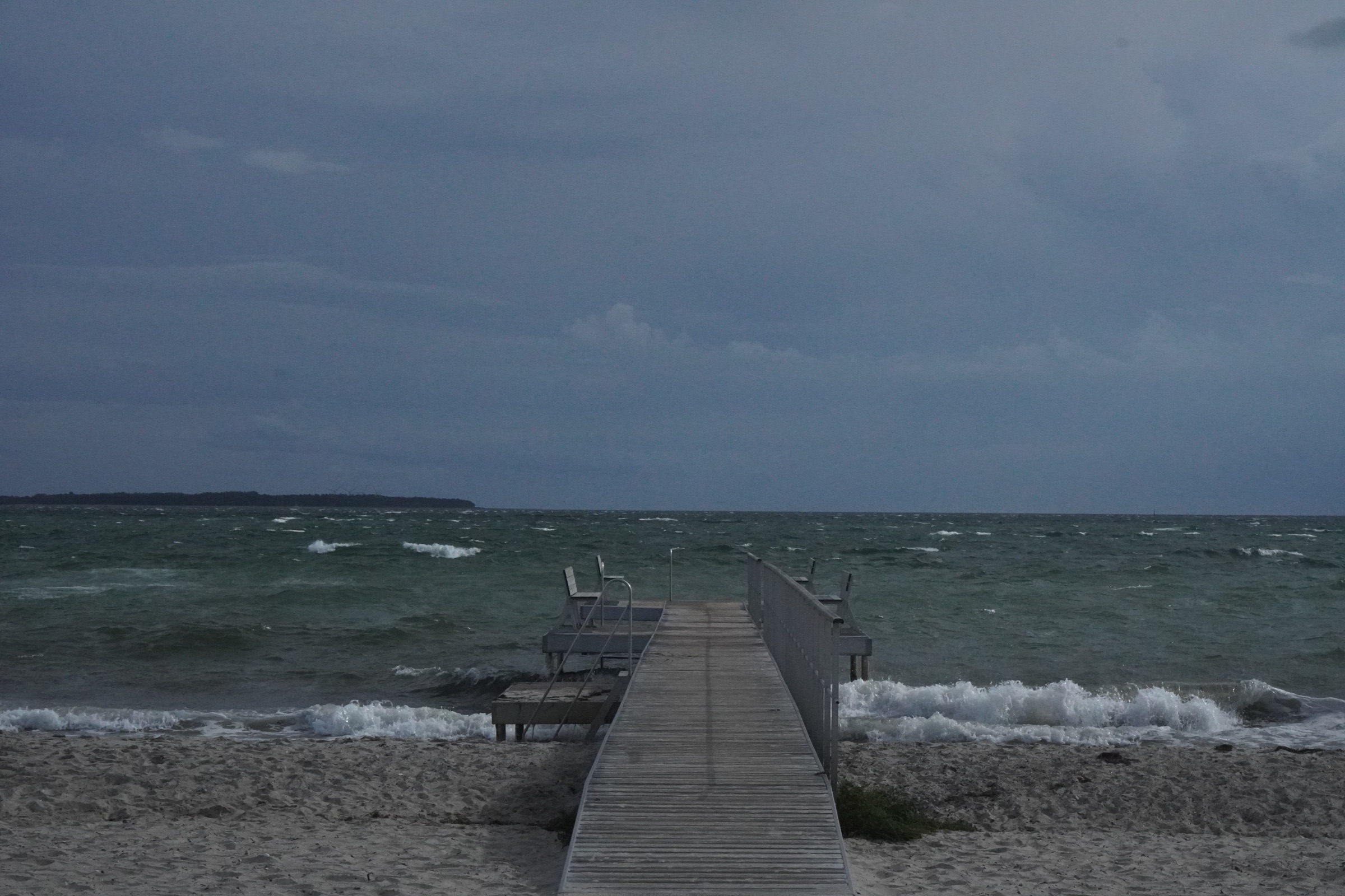 Blæsende dag ved stranden med badebro og bølger